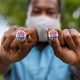 A man holds up two small pins reading "Vote 2020"